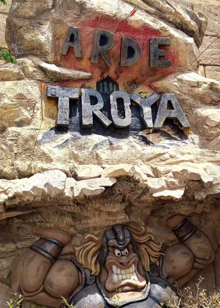The entrance sign for the 'Arde Troya' show at Terra Mítica, featuring a stylized warrior character carved into the rock.