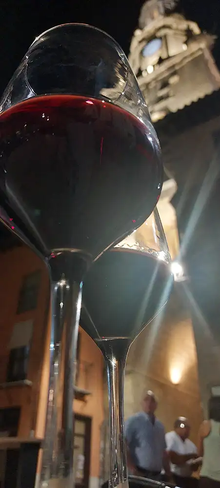 Duas taças de vinho tinto de Toro em primeiro plano com a torre do relógio da cidade iluminada ao fundo, durante a noite. Ilustra a experiência de onde comer em Toro.