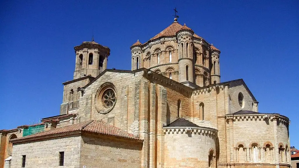Vista exterior da Colegiata de Santa María la Mayor em Toro, uma igreja românica com cúpula em escamas e telhado de telha vermelha sob céu azul, destacando sua arquitetura histórica.