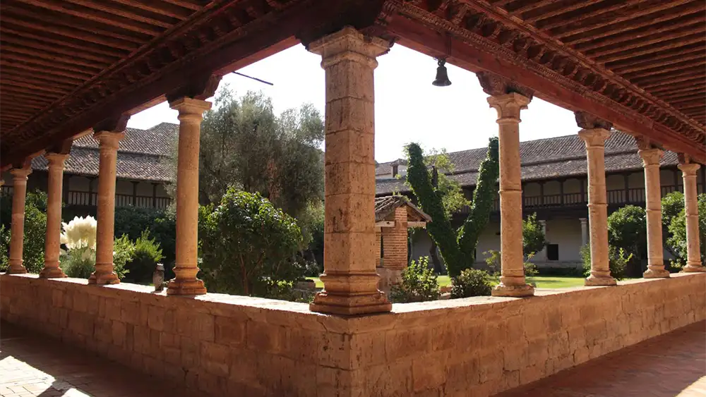 Claustro do Monasterio del Sancti Spiritus em Toro, com suas colunas de pedra, teto de madeira e vista para o pátio interno ajardinado.