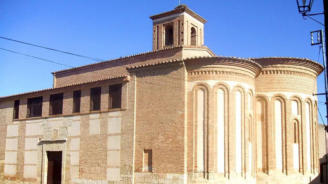 Exterior da Igreja de San Salvador de los Caballeros em Toro, destacando sua arquitetura de estilo românico-mudéjar com ábsides semicirculares de tijolo e uma torre-campanário sob o céu azul.