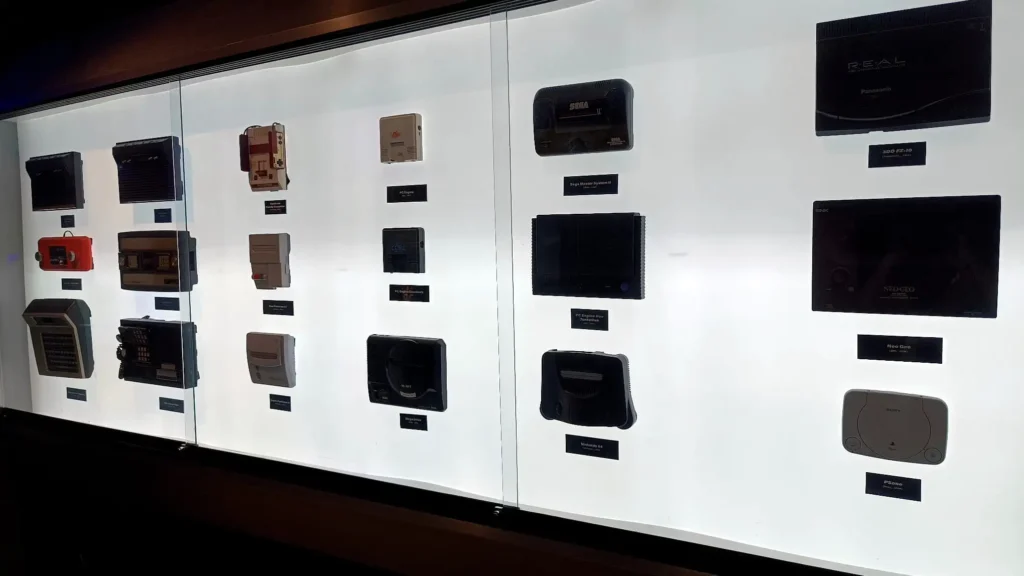 Vitrine iluminada exibindo consoles clássicos como Neo Geo, Sega, Nintendo 64 e PlayStation no OXO Madrid.
