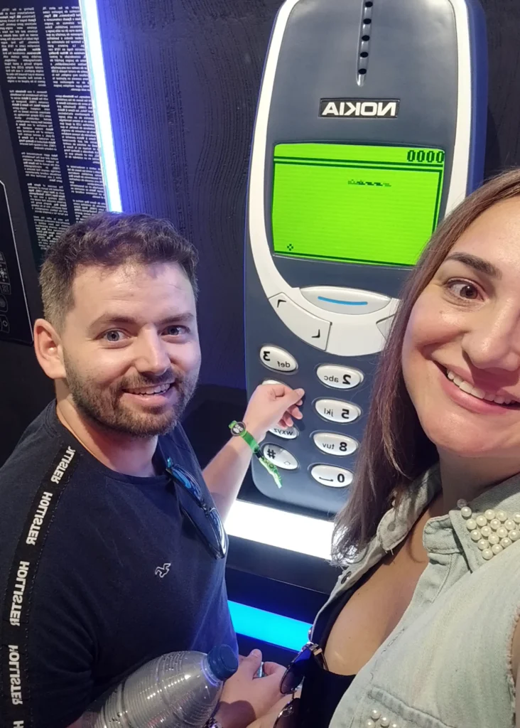 Casal posando em frente a um Nokia 3310 gigante no OXO Madrid, com jogo da cobrinha na tela.