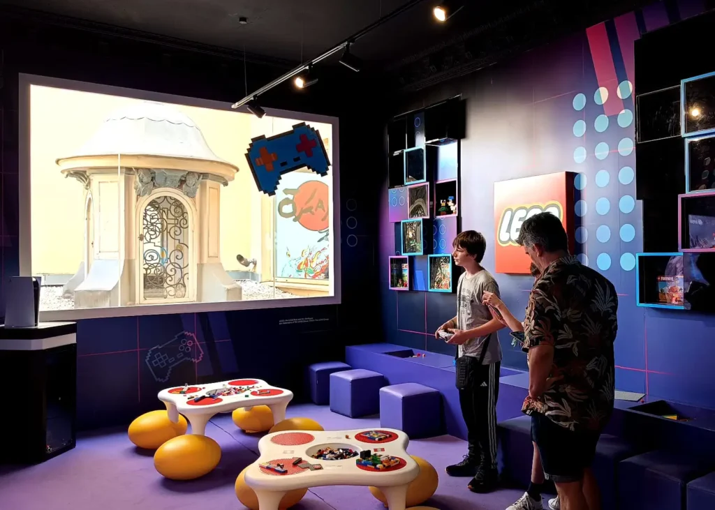 Sala interativa do OXO Madrid com mesas de Lego e adolescentes jogando videogame.