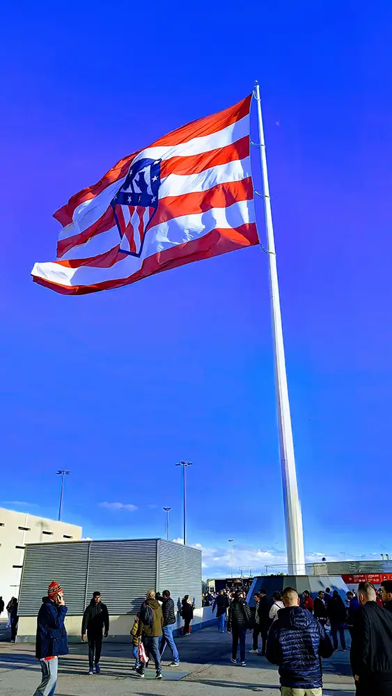 Bandeira do Atlético de Madrid tremulando ao vento diante do Estádio Metropolitano em um dia ensolarado.