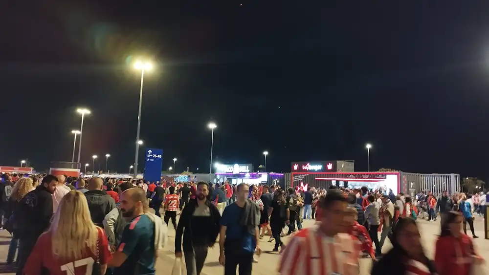 Multidão de torcedores caminhando na entrada do Estádio Metropolitano iluminado à noite.