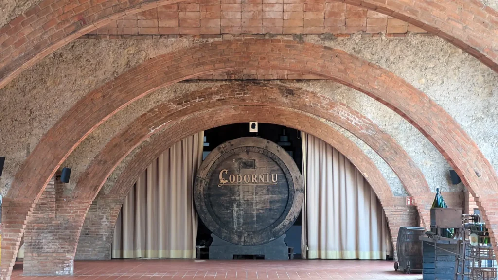 Interior das caves da Codorníu com arcos de tijolo e grande barril histórico ao centro