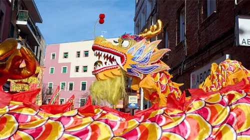 Desfile do Ano Novo Chinês com dragão colorido ocupando a rua, durante celebração em bairro urbano da Espanha.