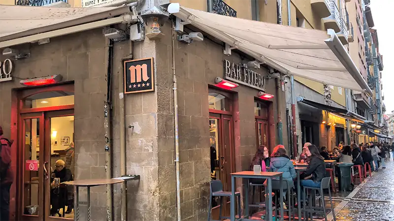 Bar Fitero na Calle Estafeta, em Pamplona, com mesas altas na calçada e pessoas sentadas no exterior.