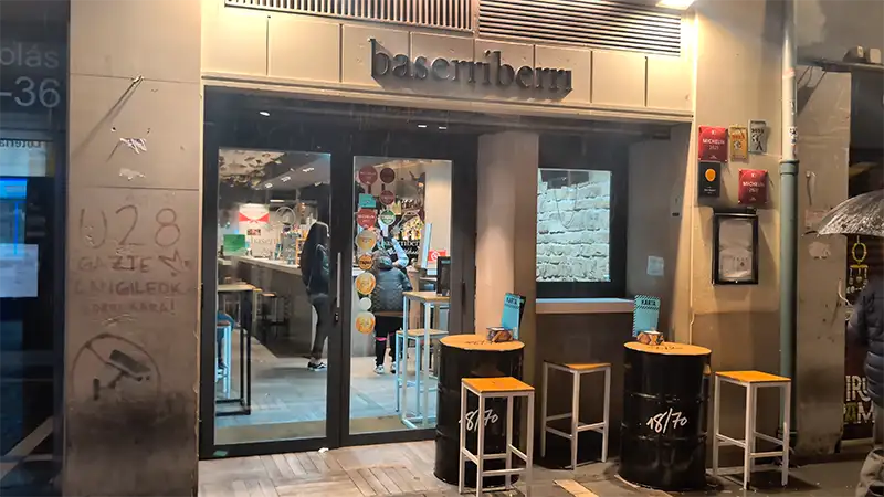 Fachada do bar Baserriberri em Pamplona, com mesas altas no exterior e interior visível através da porta de vidro.