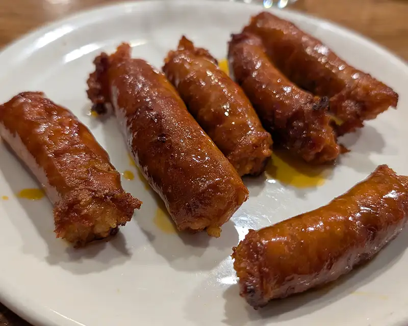 Chistorra frita servida em pedaços sobre prato branco, típica dos bares de Pamplona e da gastronomia de Navarra.