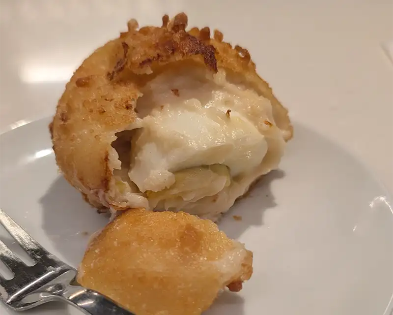 Frito de ovo típico de Pamplona, croquete grande empanado e aberto, com interior cremoso, servido em prato branco.