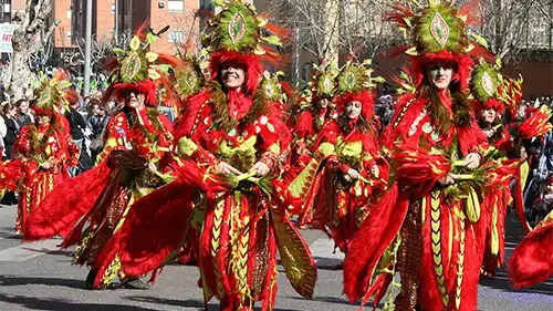 Desfile de carnaval em Badajoz com grupo fantasiado em tons de vermelho e dourado, dançando pelas ruas durante a celebração.