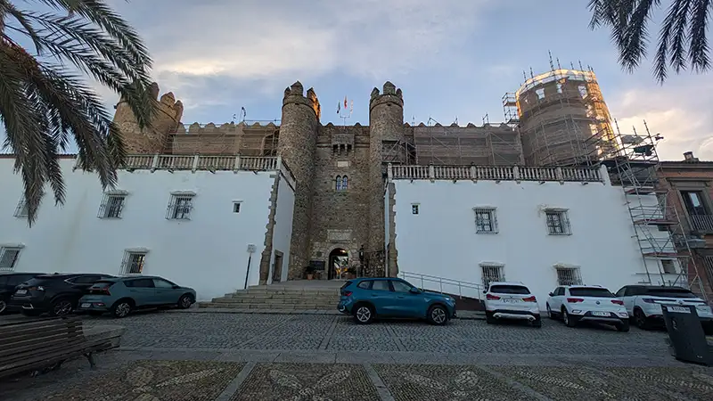 Fachada do Alcázar de los Duques de Feria, em Zafra, com as torres centrais em pedra e o edifício histórico ao fundo.