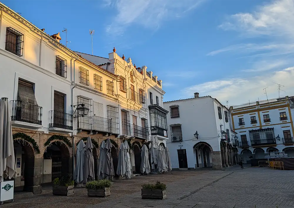 Casas brancas com arcadas e varandas na Plaza Chica de Zafra, no início da manhã, com esplanadas fechadas e luz suave.