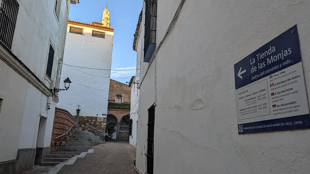 Entrada do Convento de Santa Clara, em Zafra, com rua estreita, escadas de acesso e sinalização na parede indicando a loja das monjas.