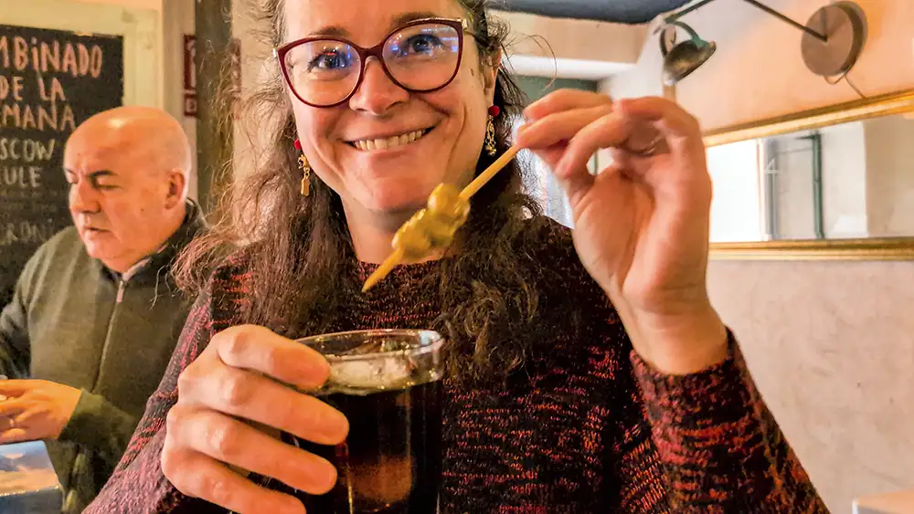 Mulher segura copo de vermut com azeitona no palito em bar de tapas em Toledo.