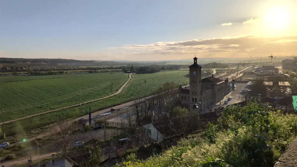 Vista panorâmica de Toledo ao entardecer com a estação de trem e o rio Tejo ao fundo, paisagem da região de Castilla-La Mancha.