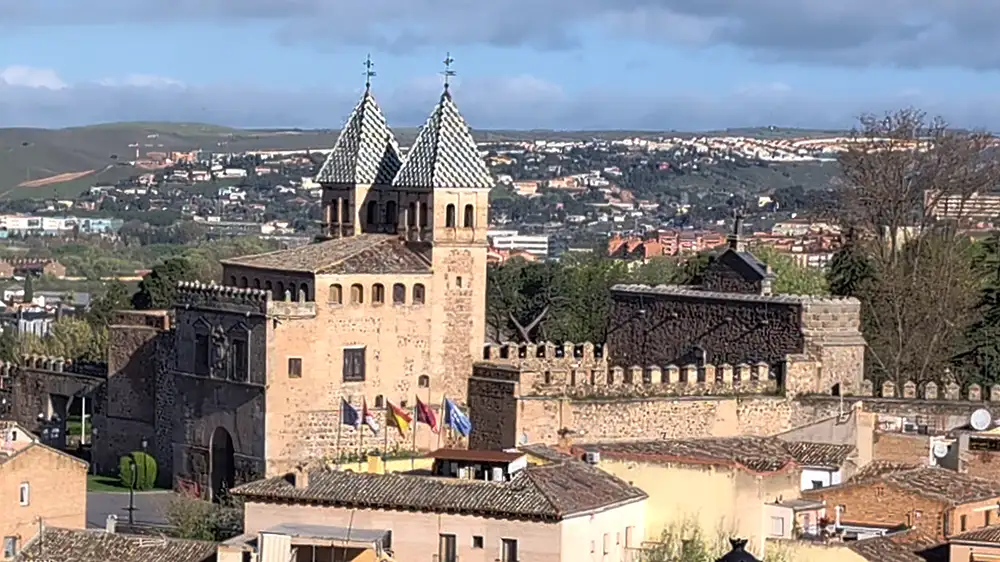 Vista da Puerta de Bisagra e muralhas de Toledo com bandeiras e cidade ao fundo.