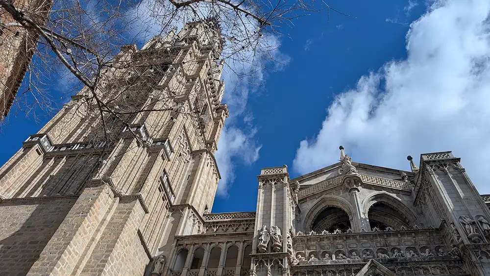 Fachada e torre da Catedral de Toledo vista de baixo contra o céu azul.
