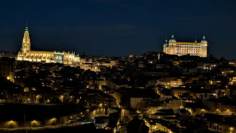 Vista panorâmica de Toledo à noite com Catedral e Alcázar iluminados.