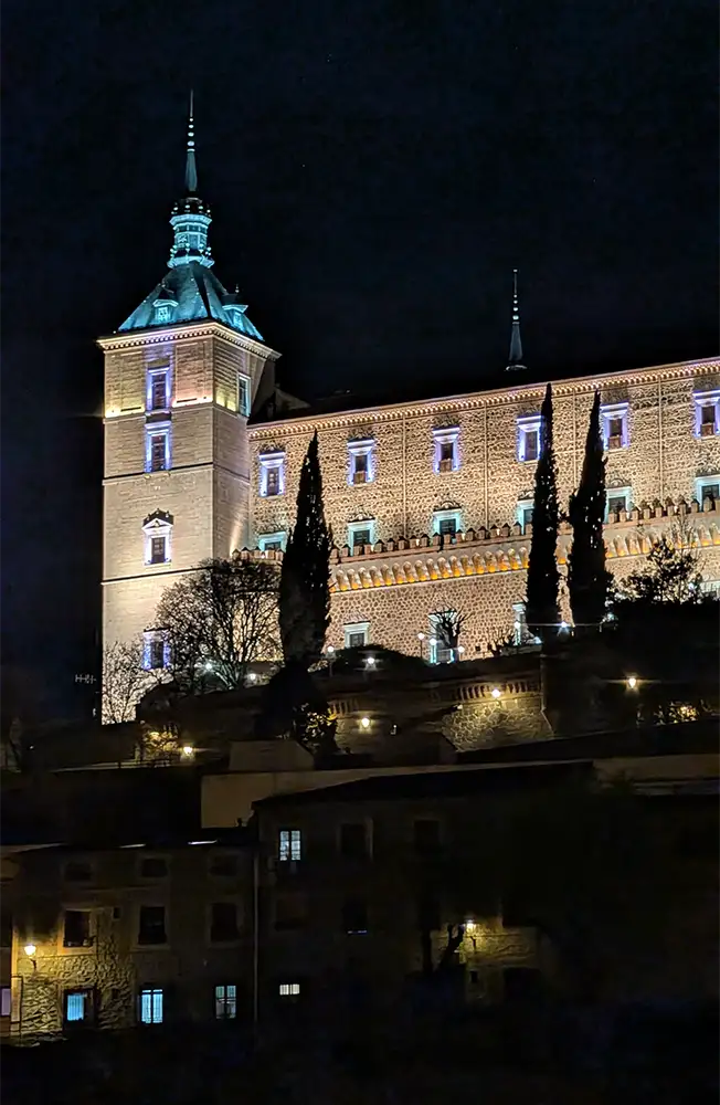 Alcázar de Toledo iluminado à noite visto de baixo com céu escuro.