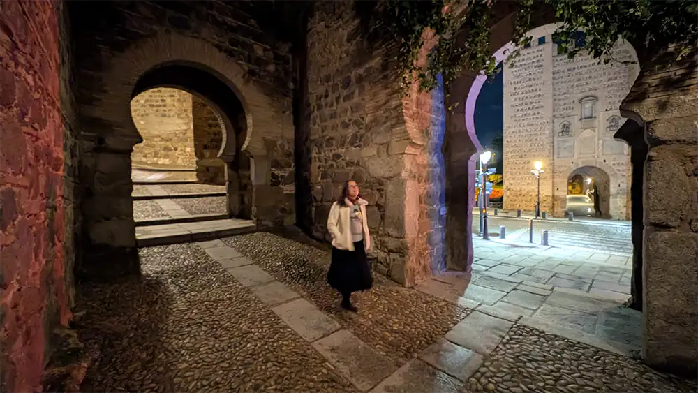 Porta árabe iluminada à noite no centro histórico de Toledo com muralhas ao fundo.