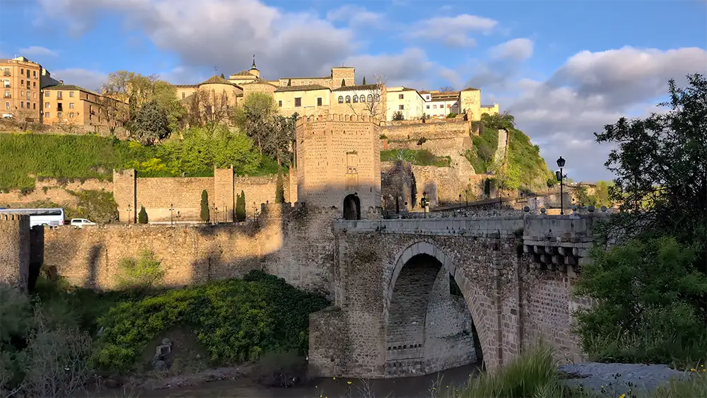 Puente de Alcántara em Toledo com muralhas históricas e entrada da cidade ao fundo.