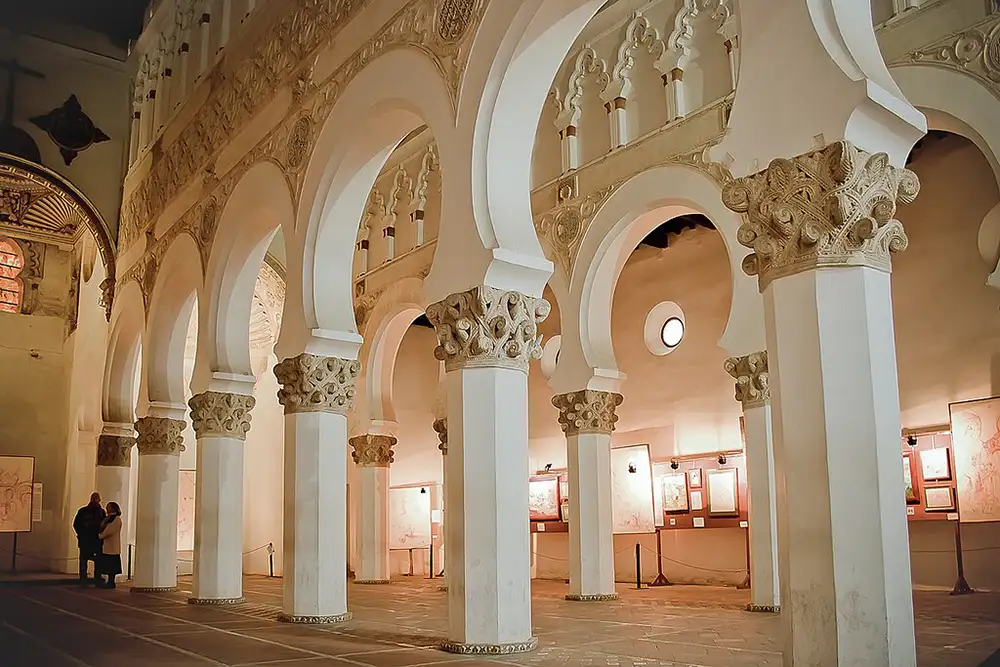 Interior da Sinagoga de Santa María la Blanca em Toledo com arcos brancos e colunas decoradas.