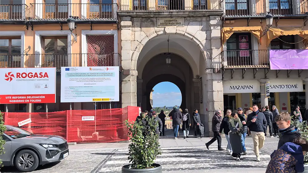 Arco de entrada da Plaza de Zocodover em Toledo com visitantes e comércio ao redor.