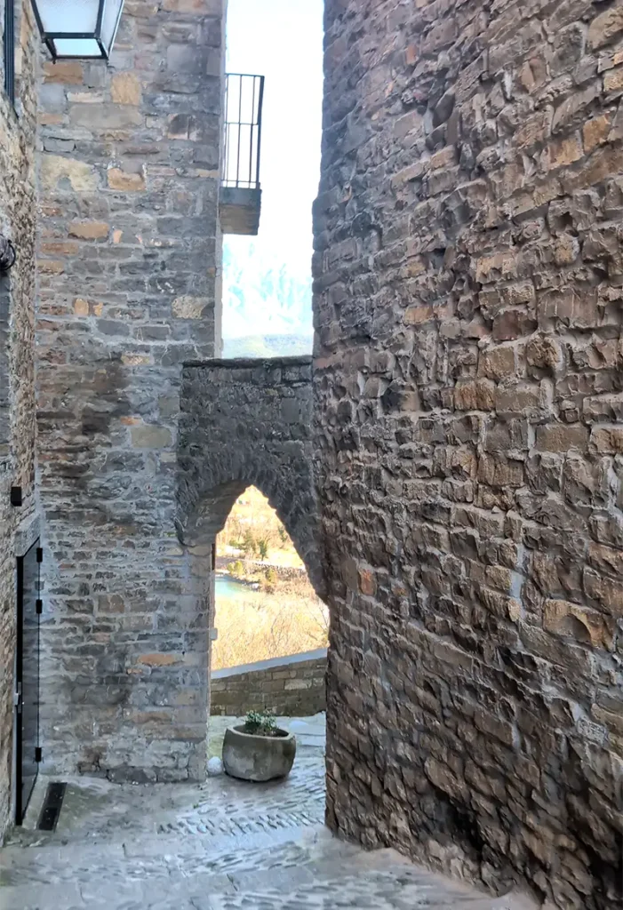 Ruela estreita de pedra em Aínsa com arco medieval e vista para o vale e as montanhas ao fundo, Huesca, Aragão.