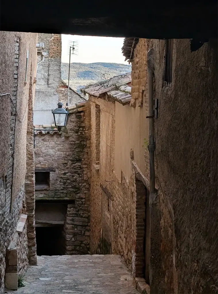 Ruela estreita de pedra em Alquézar com casas medievais e vista para o vale ao fundo, Huesca.