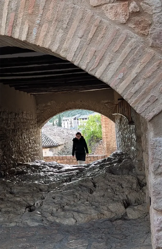 Mulher caminhando por uma passagem em arco de pedra nas ruelas do centro histórico de Alquézar, Huesca.