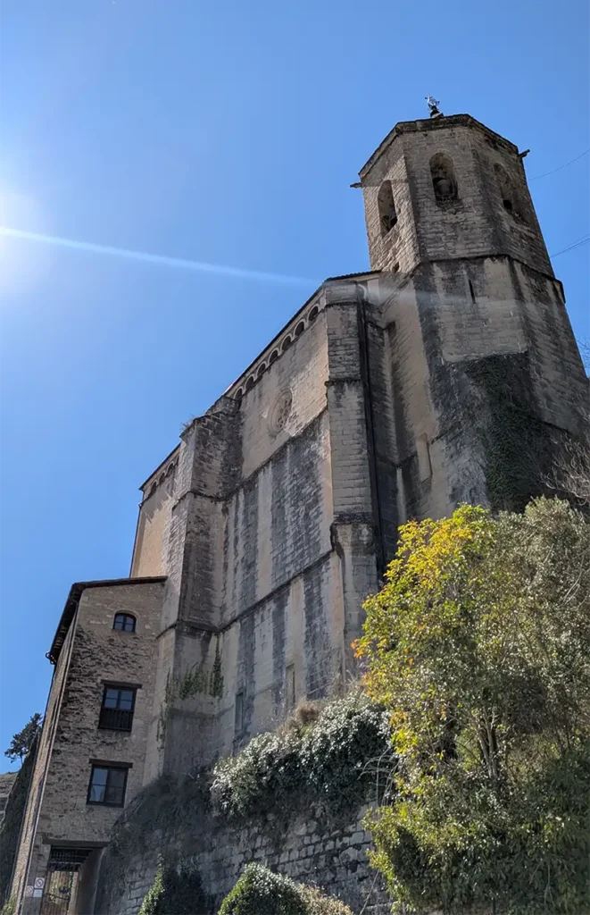 Igreja de pedra de Graus vista de baixo com torre sineira e céu azul ao fundo, Huesca, Aragão.