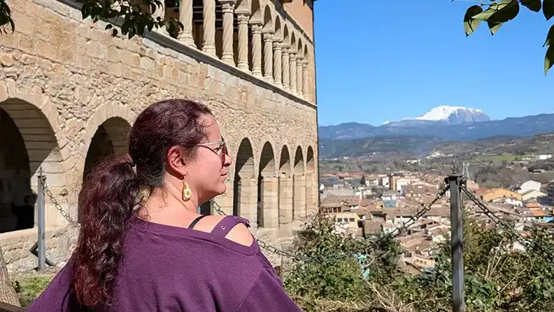 Mulher observando a vista do Santuario de la Virgen de la Peña em Graus, com a cidade e uma montanha nevada dos Pirineus ao fundo, Huesca.