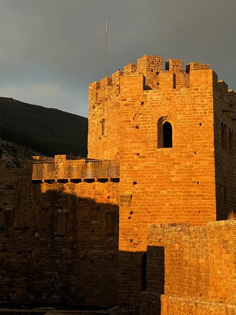 Torre principal do Castillo de Loarre iluminada pela luz dourada do pôr do sol com céu nublado ao fundo, Huesca, Aragão.