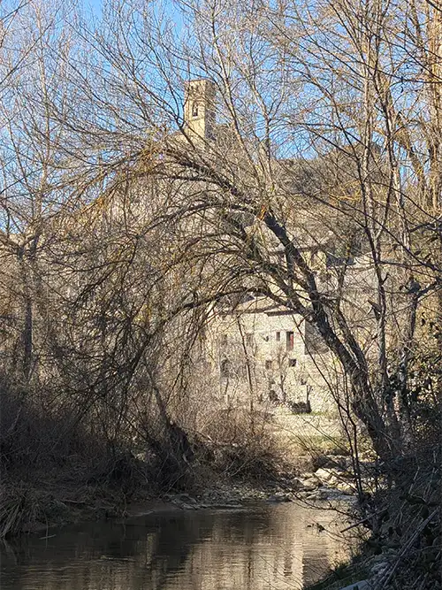 Rio com reflexo das árvores e o povoado medieval de Montañana visível ao fundo com a torre da igreja, Huesca, Aragão.
