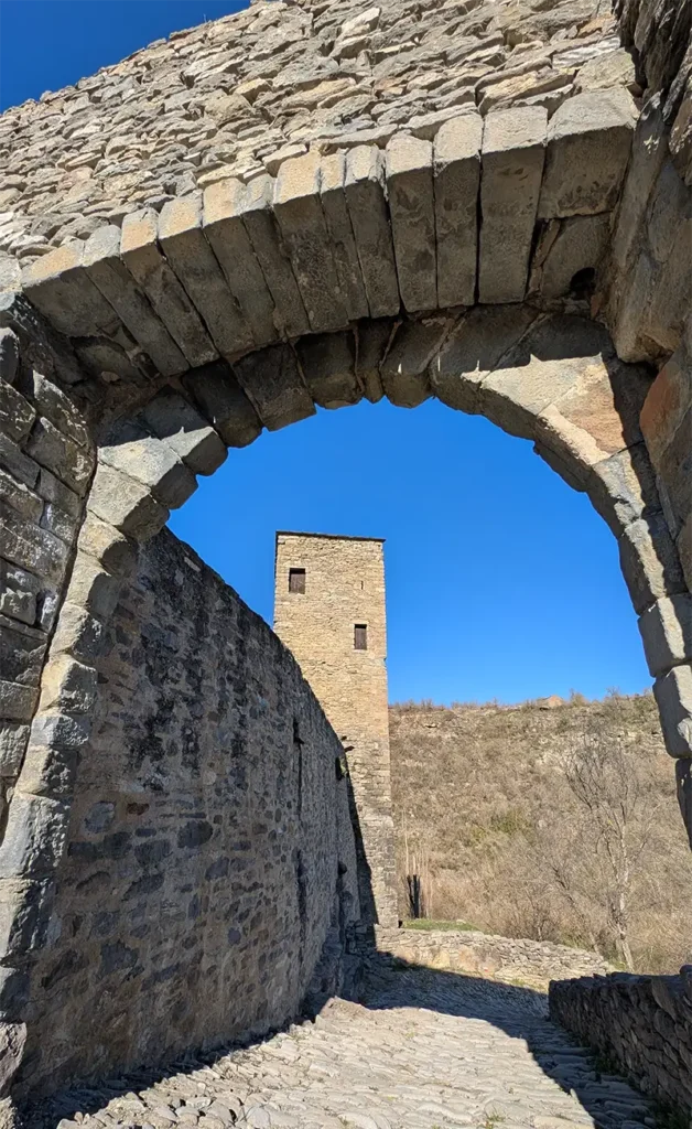 Arco de pedra medieval em Montañana com a Torre de la Mora ao fundo e céu azul, Huesca, Aragão.