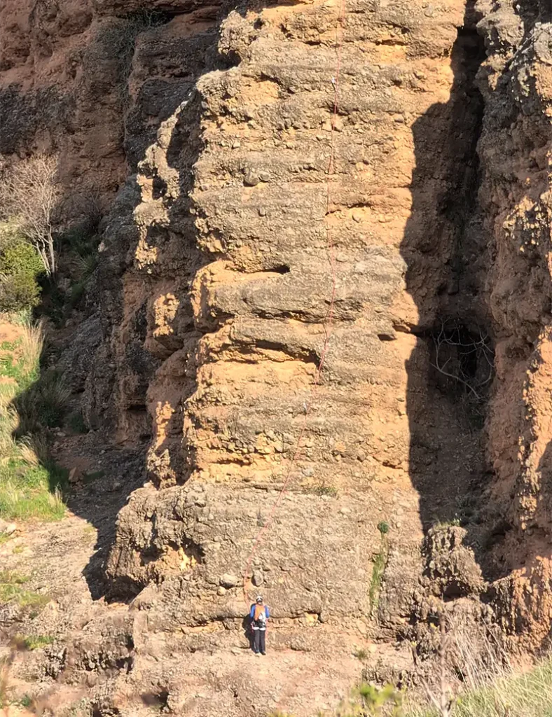 Escalador solitário na base de um dos mallos de Riglos, com a formação rochosa ocupando quase toda a imagem, Huesca, Aragão.