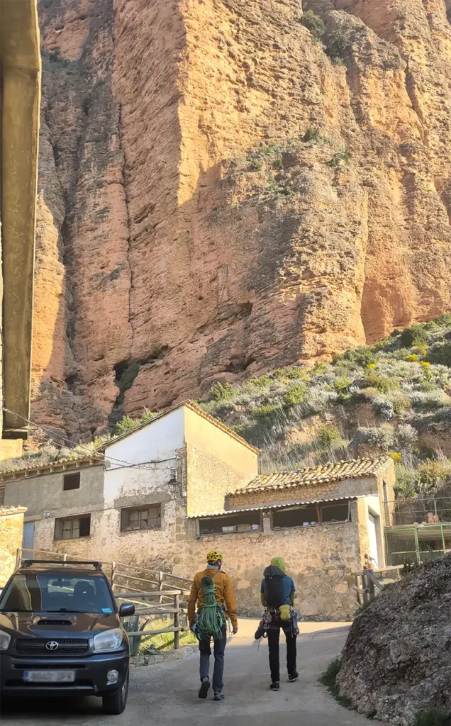 Dois escaladores equipados com cordas e capacetes caminhando em direção aos mallos de Riglos, Huesca, Aragão.