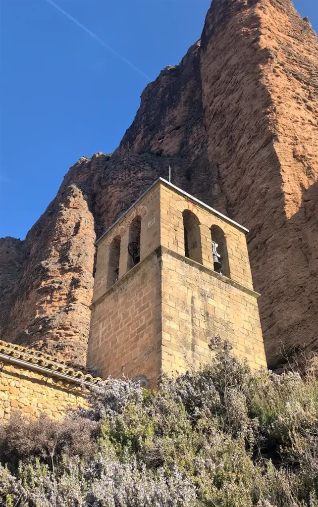 Torre sineira da igreja de Riglos com um dos mallos de rocha vermelha dominando o fundo, Huesca, Aragão.