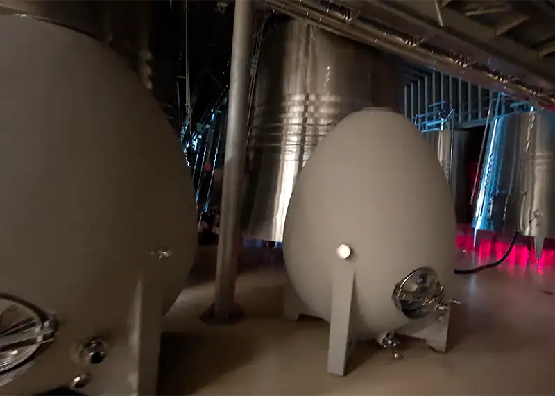 Uma fileira de tanques de fermentação ovais de concreto, conhecidos como "ovos de concreto", alinhados em uma área de produção moderna na Bodega Portia, sob iluminação focalizada.