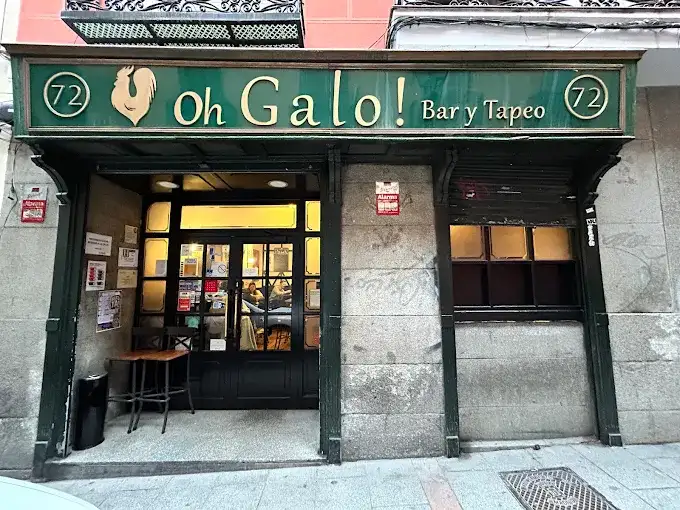 Fachada de estilo clássico do bar Oh Galo! em Madrid com letreiro verde em madeira dourada e portas de vidro.