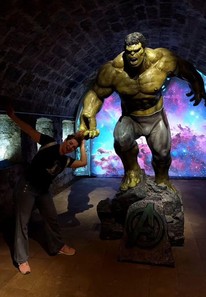 Escultura do personagem Hulk em pose de ataque sobre uma base dos Vingadores em corredor de pedra com fundo galáctico.