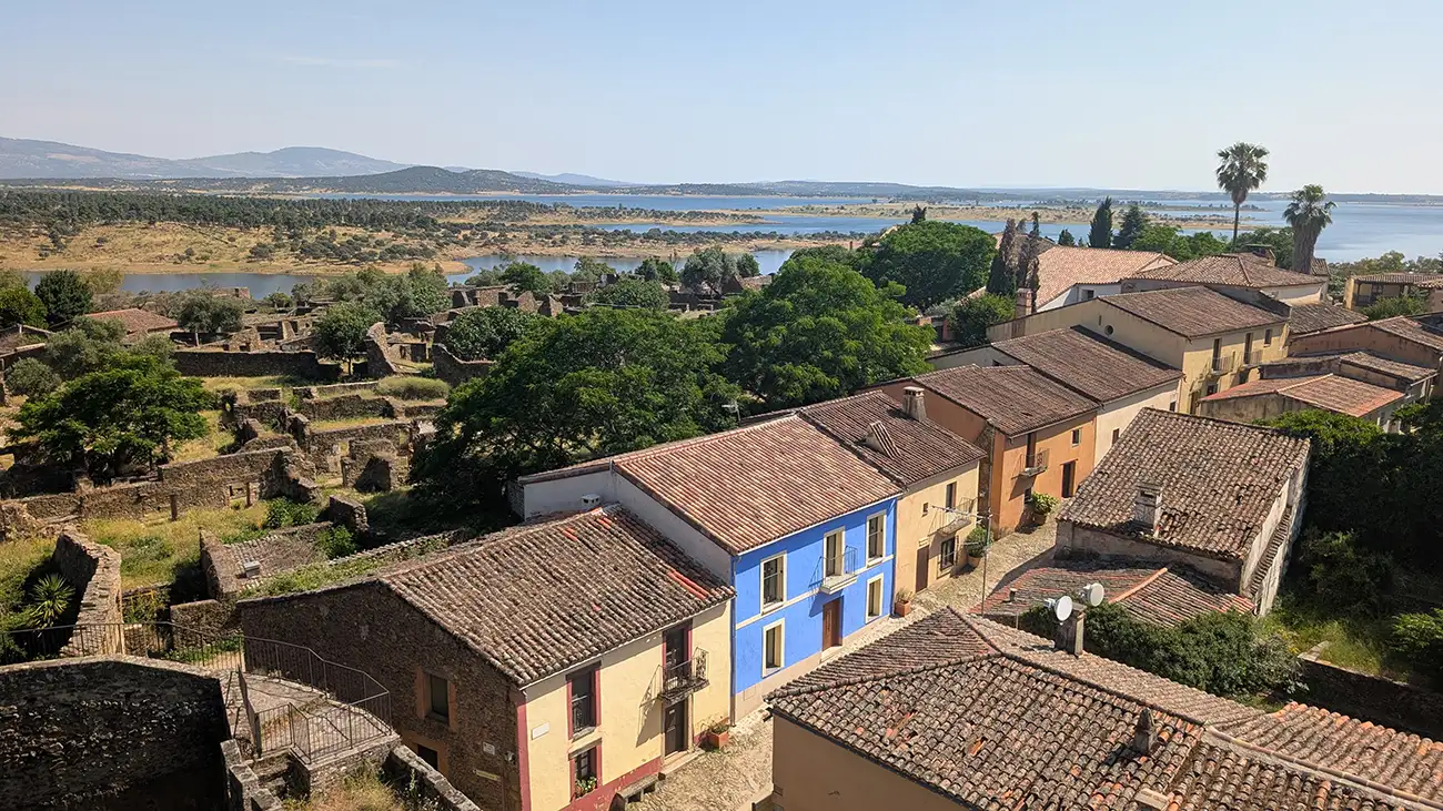 Vista aérea de Granadilla mostrando casas con tejados de arcilla, una fachada azul, ruinas y el embalse al fondo.