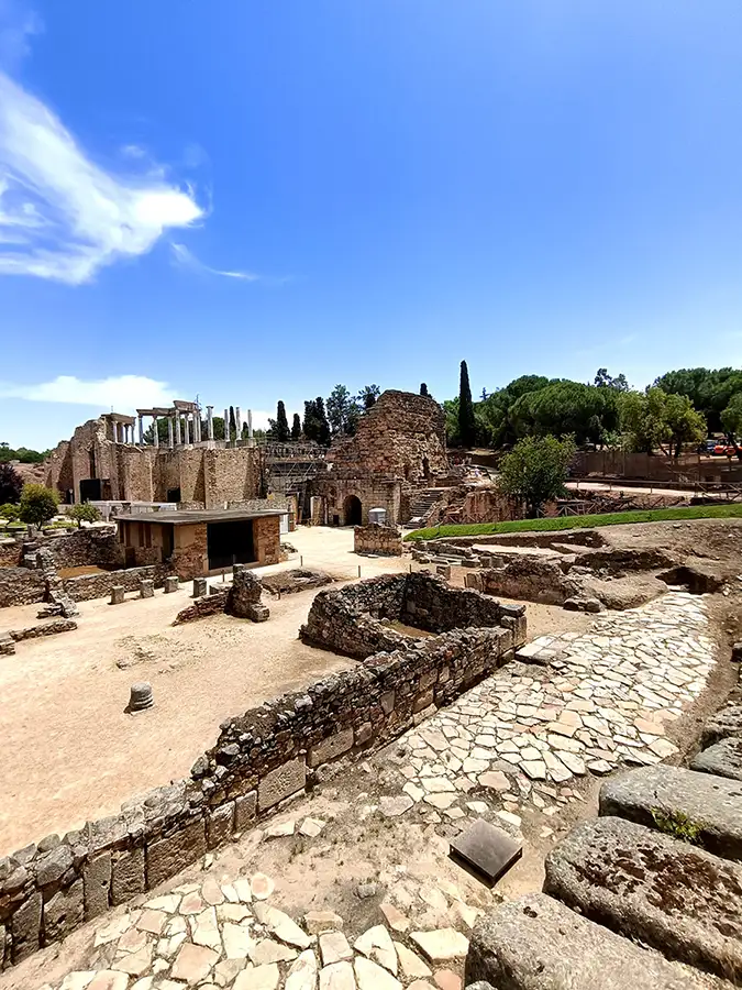 Vista elevada das ruínas do conjunto arqueológico de Mérida com as colunas do Teatro Romano ao fundo e céu azul