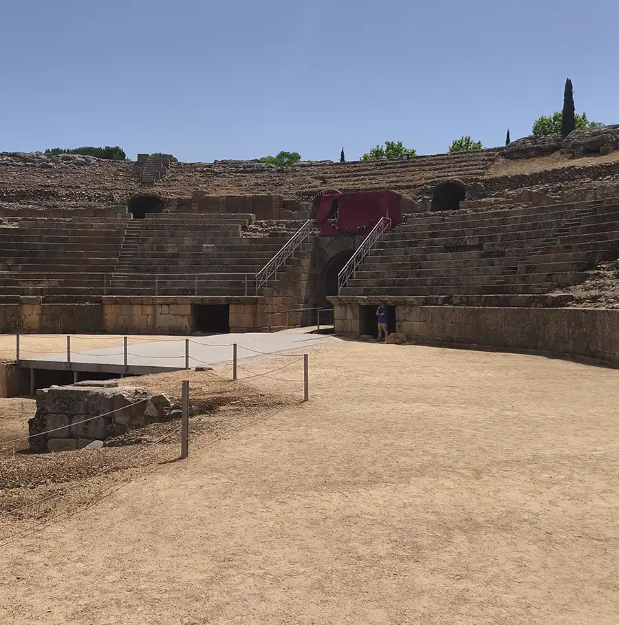 Vista frontal das arquibancadas de pedra do Anfiteatro Romano de Mérida com acesso central e vegetação ao fundo