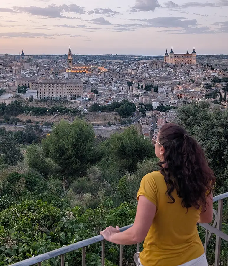 Mulher observando a vista panorâmica de Toledo ao entardecer a partir da varanda do Parador, com a Catedral e o Alcázar ao fundo