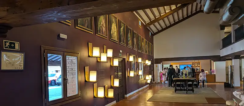 Saguão do Parador de Toledo com pinturas na parede, vigas de madeira no teto e iluminação quente