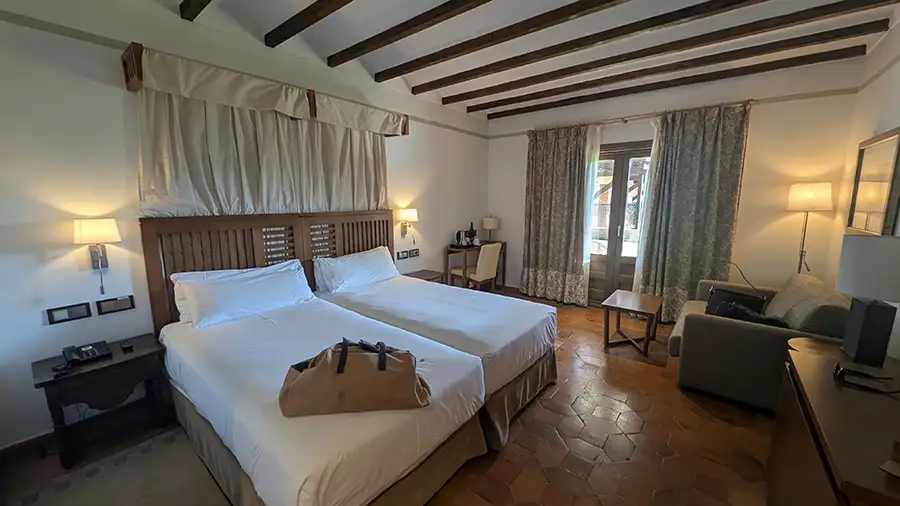 Quarto do Parador de Toledo com cama de casal, piso de barro, vigas no teto e porta com acesso direto ao jardim